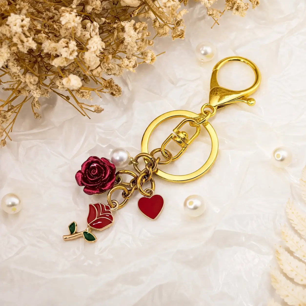 Gold keychain with red flower pendant, pearl accents, and floral details, featuring the Rose Bag Charm Keychain by Hypes Inventory.