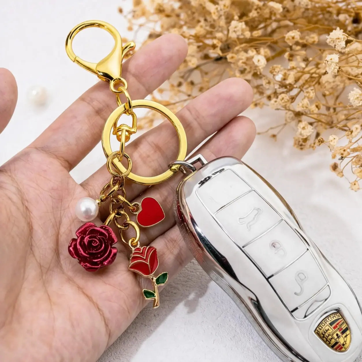 Gold rose bag charm keychain with red flower pendant and pearls, designed for accessorizing bags and keys.